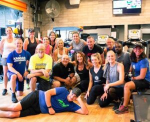 Group of members and coaches posing together inside Results Only Fitness gym in Phoenix after a training session, surrounded by cardio equipment and a supportive community atmosphere.