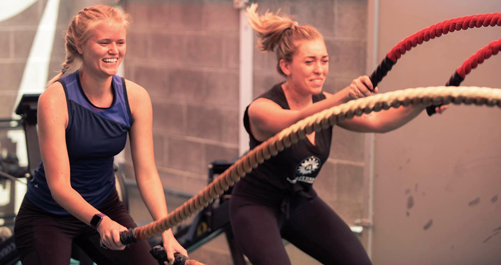 Two women using battle ropes during a group fitness workout at Results Only Fitness gym.